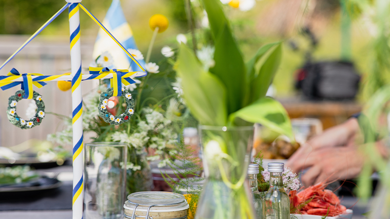 Midsommarbord med majstang, blommor och sillburkar